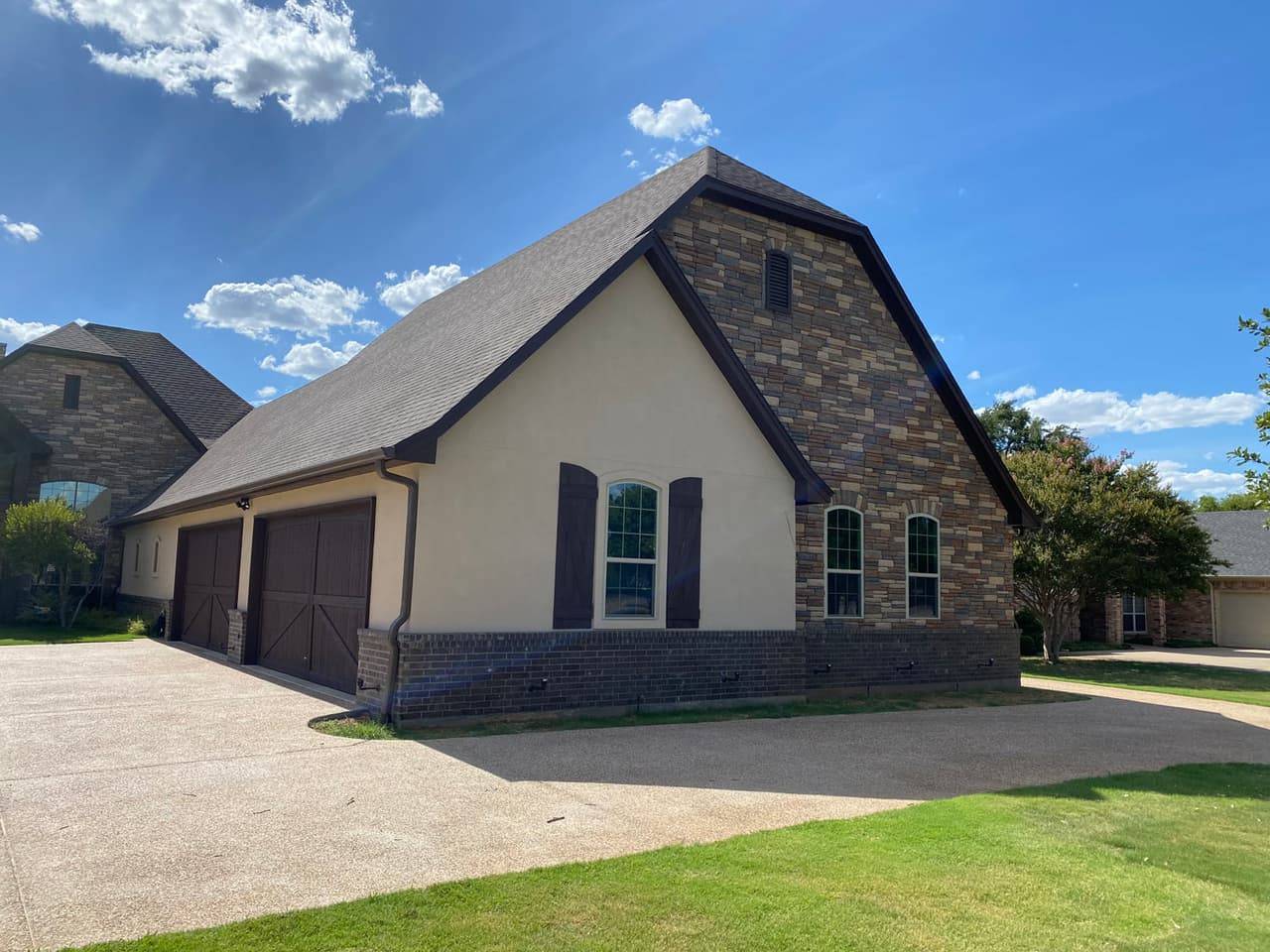 Home exterior with stucco, stone and brick, wood shutters and a three-car garage