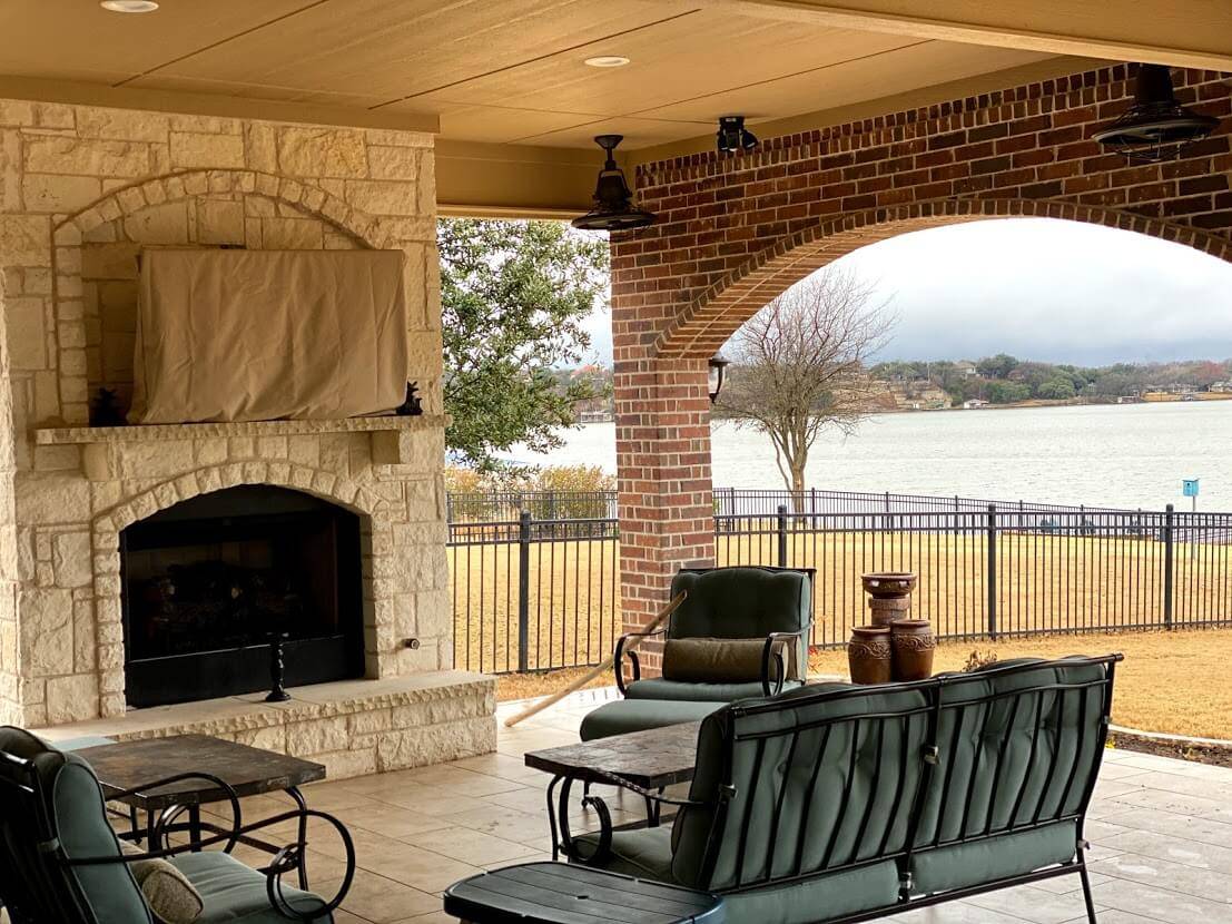 Covered patio with a stone fireplace and a brick arch looking out to a lake