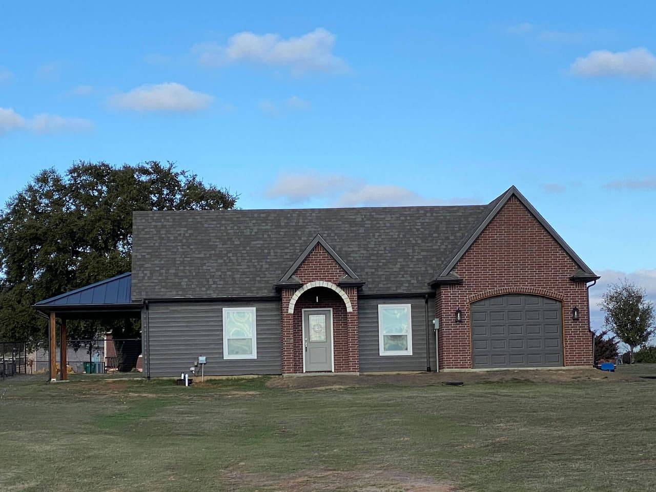 Gray-sided home with a brick entry arch, a brick garage and a metal-roof carport on the side