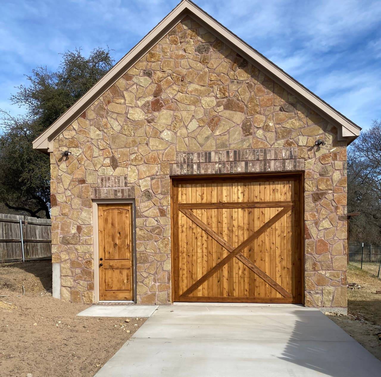 Custom stone garage with a stained cedar garage door and matching side door, built by Custom Building & Remodeling in Granbury, TX