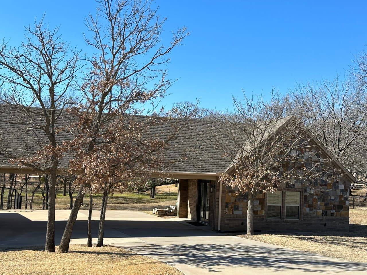 Stone and brick home with a long carport and bare oak trees in the yard