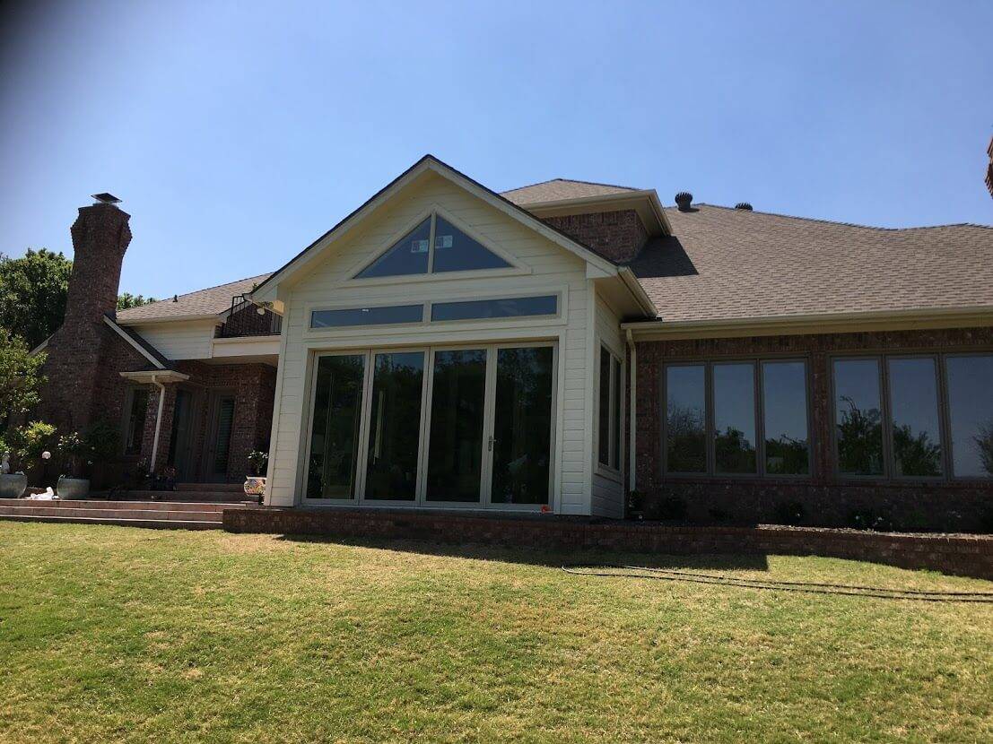 Gabled addition on the back of a brick home with a wall of glass doors, a triangular window and a row of transom windows