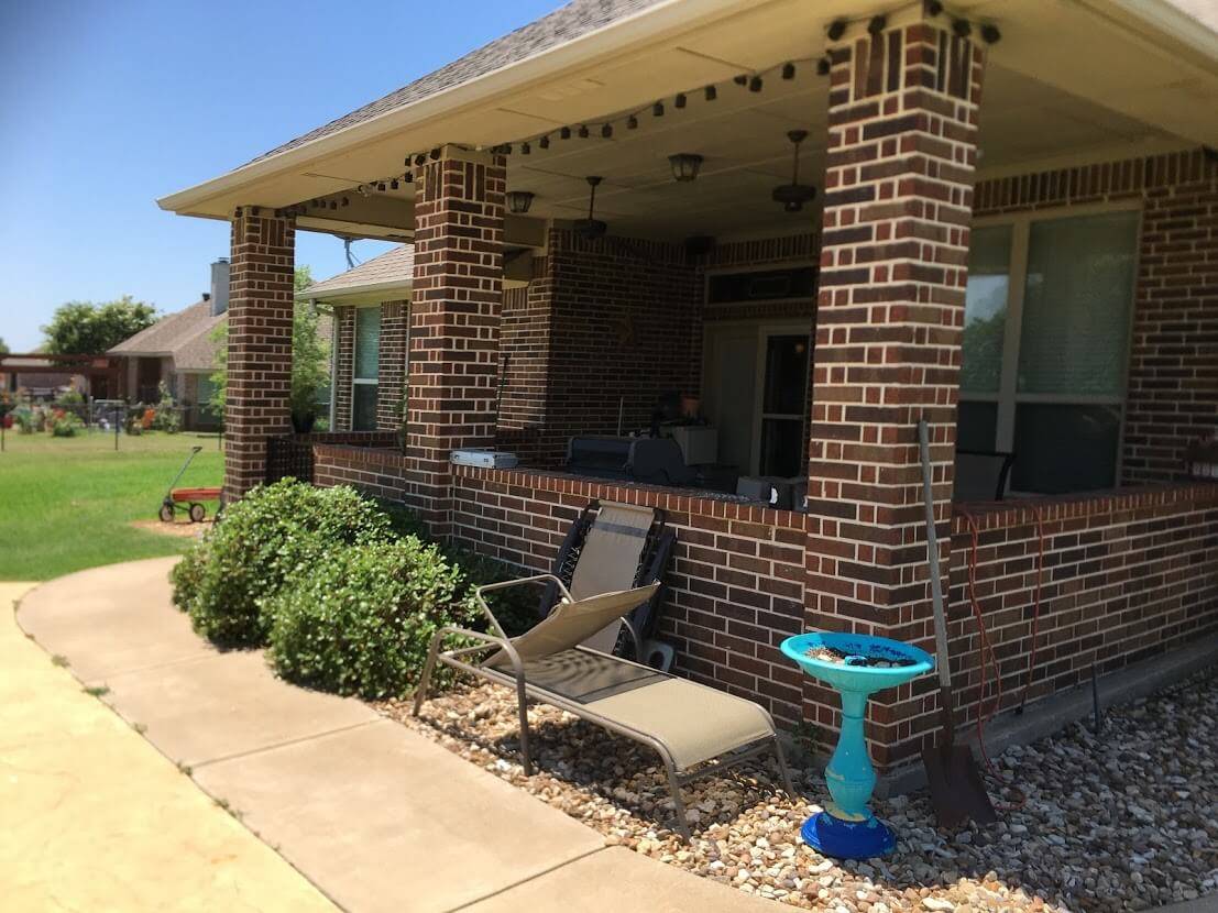 Covered patio with brick columns, a low brick wall and string lights along the back of a brick home