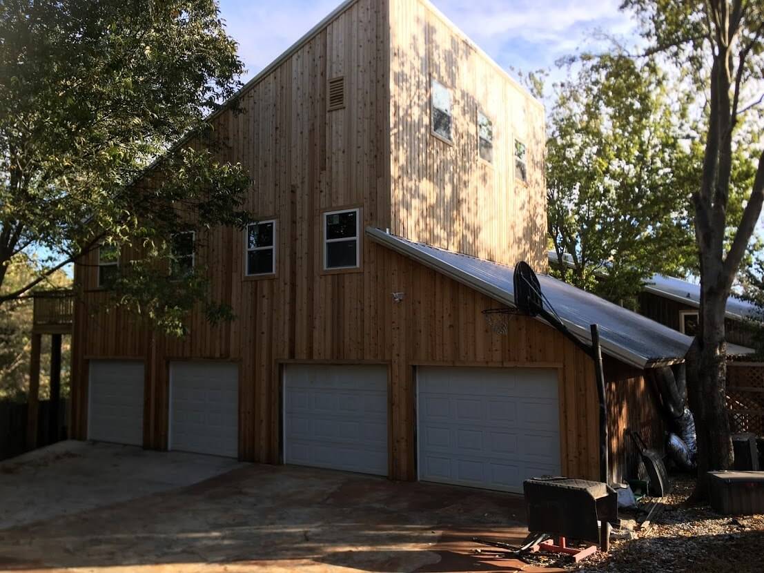 Tall cedar-sided building with four garage doors, upper windows and a metal roof